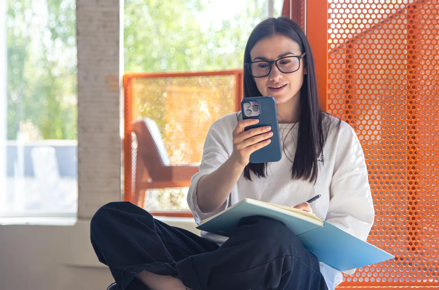 Woman using smartphone and notebook indoors for work or study.