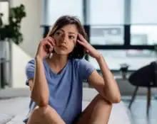 Woman sitting on bed, looking thoughtful and contemplative in a modern bedroom setting.