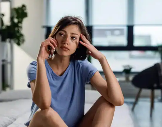 Woman sitting on bed, looking thoughtful and contemplative in a modern bedroom setting.