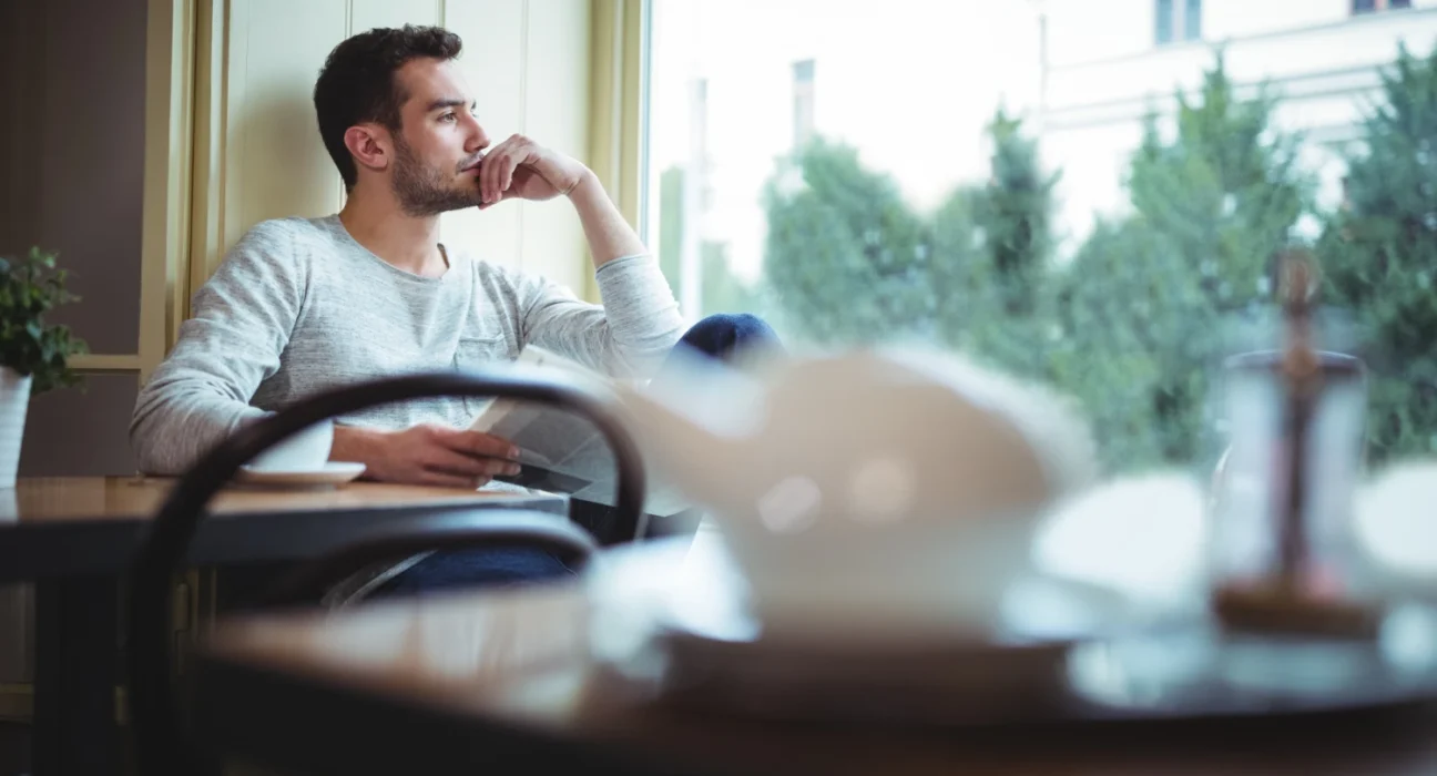 Man sitting alone by the window, deep in thought, contemplating missed opportunities.