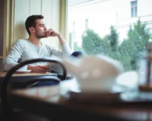 Man sitting alone by the window, deep in thought, contemplating missed opportunities.