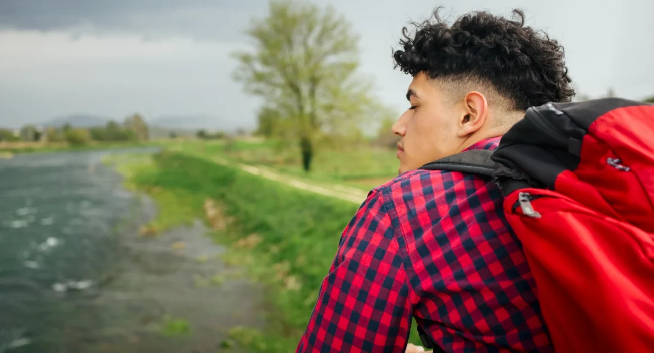 Young man with backpack looking at nature, embracing late start in life.