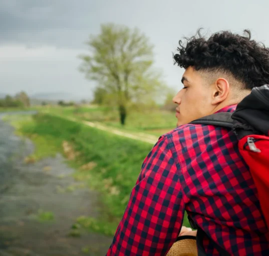 Young man with backpack looking at nature, embracing late start in life.