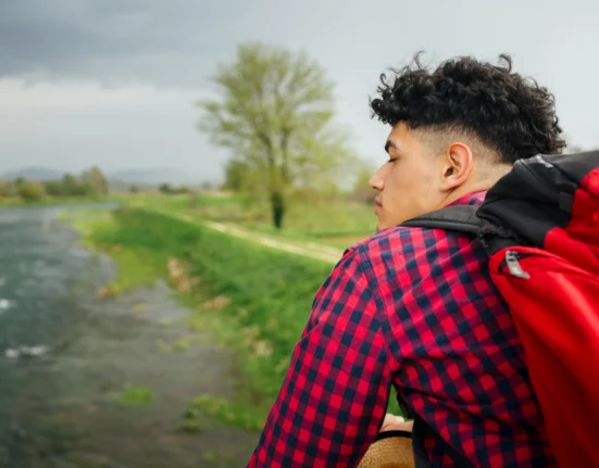 Young man with backpack looking at nature, embracing late start in life.