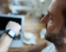Man looking at his smartwatch while working on a laptop, emphasizing the importance of time manageme.