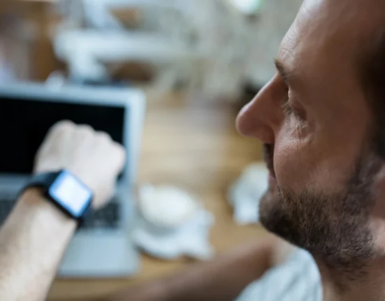 Man looking at his smartwatch while working on a laptop, emphasizing the importance of time manageme.