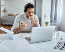 Man struggling with multiple tasks on his laptop, showing stress and frustration.