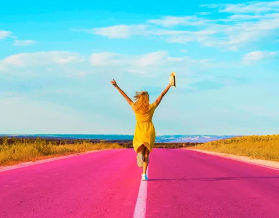 Woman running on a vibrant pink road with arms raised in joy and freedom.