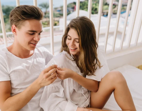 Young couple smiling and sharing a happy moment on a balcony with a city view.