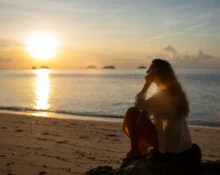 Sunset reflection on the ocean with a woman sitting on the beach, embracing self-love and personal g.