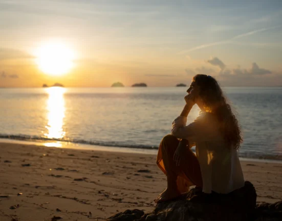 Sunset reflection on the ocean with a woman sitting on the beach, embracing self-love and personal g.