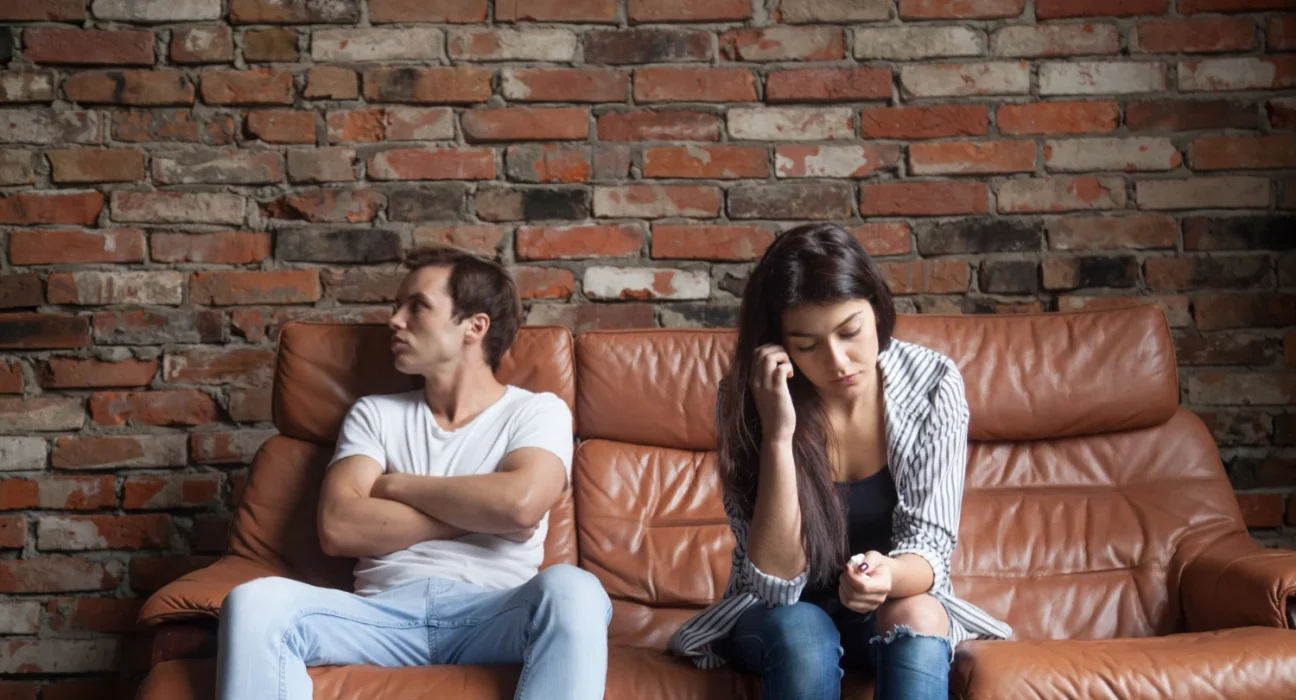 Couple sitting apart on a sofa, showing emotional distance after a breakup.