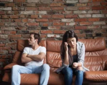 Couple sitting apart on a sofa, showing emotional distance after a breakup.