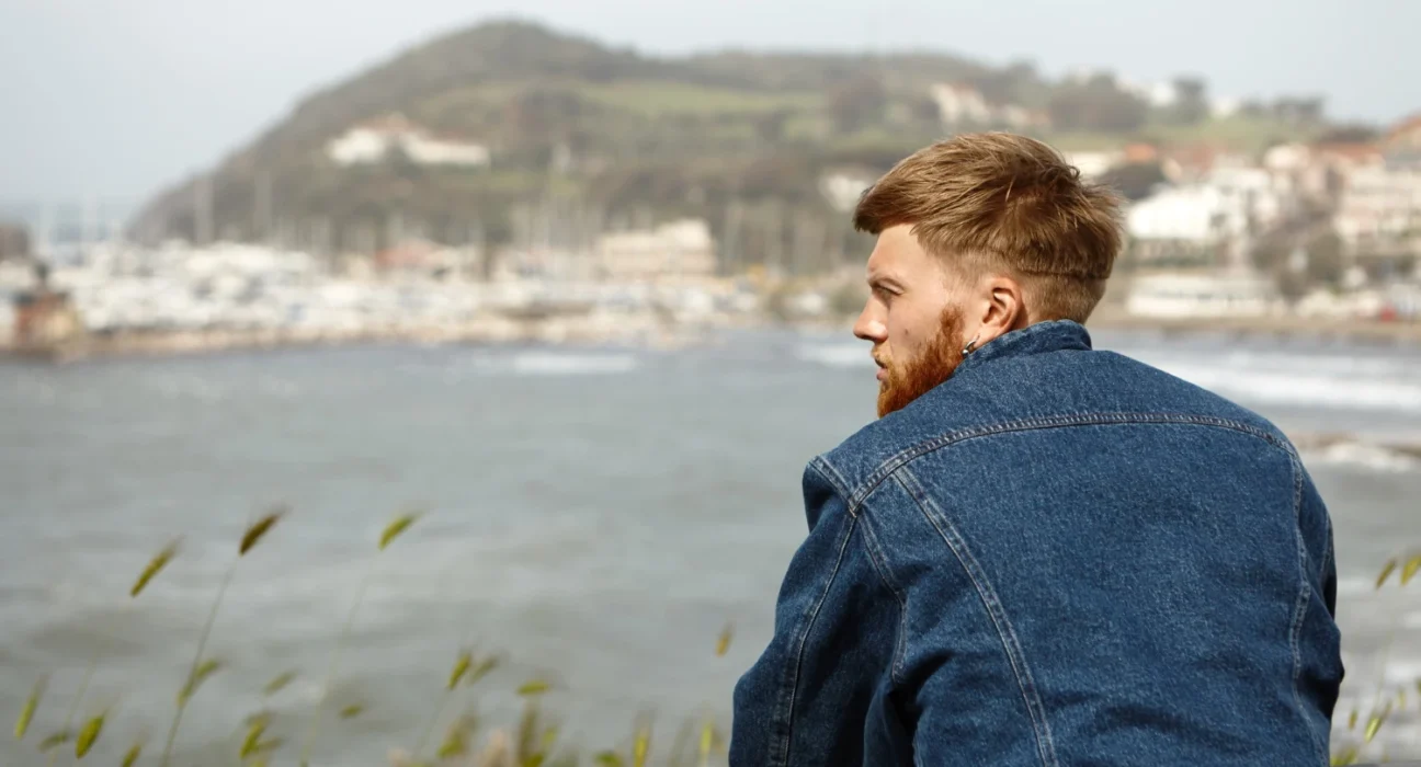 Young man contemplating by the water, symbolizing resilience after loss and discovering new opportun.
